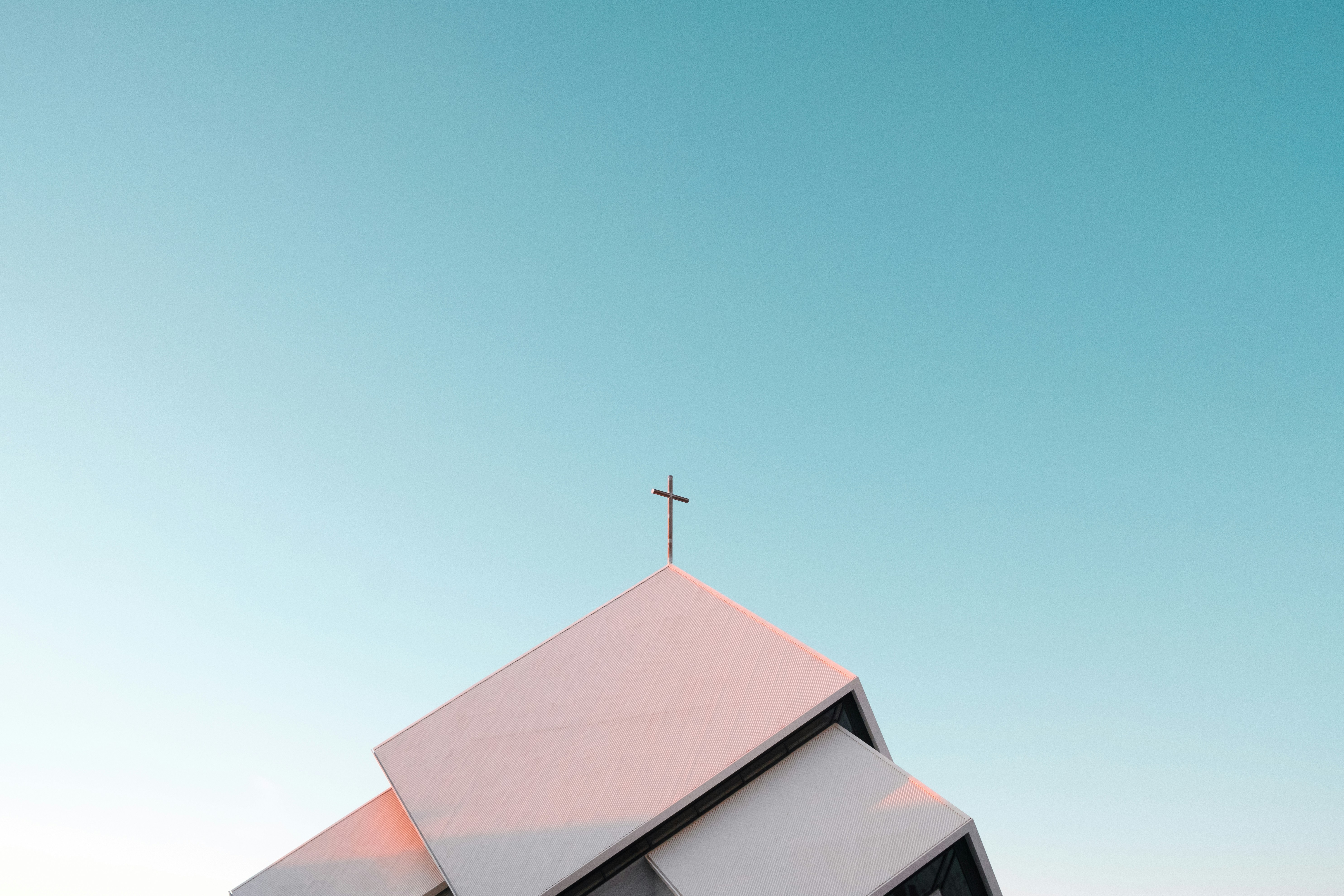 A church roofline with a cross silhouetted against a clear blue sky